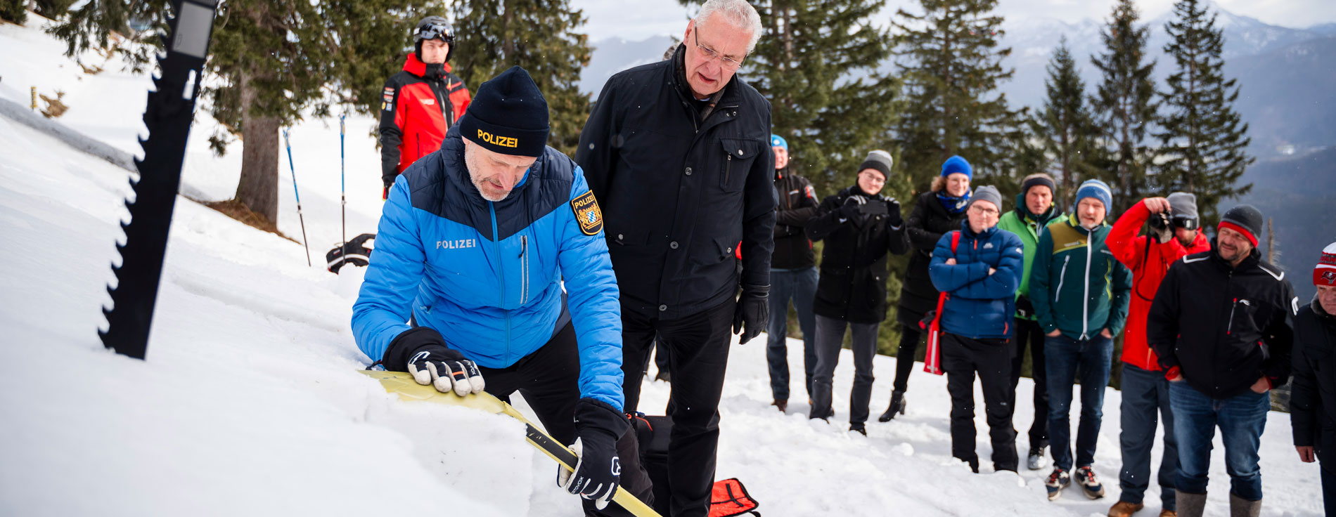 Innenminister Herrmann und Einsatzkräfte, u.a. ein Polizist, mit Lawinenschaufeln im Schnee